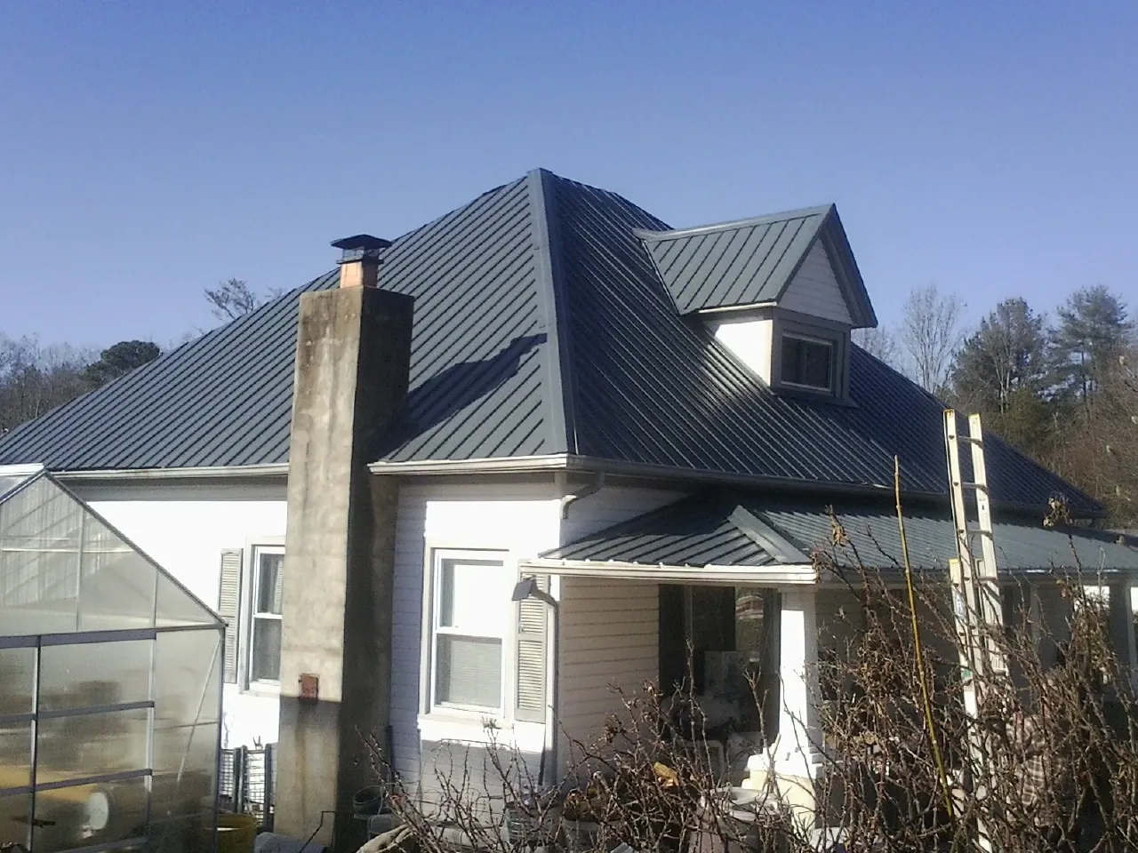 Dark blue standing seam metal roof on a white farmhouse with dormer — Slate & Tile Roof Repair by Roofing Brothers in Forestdale