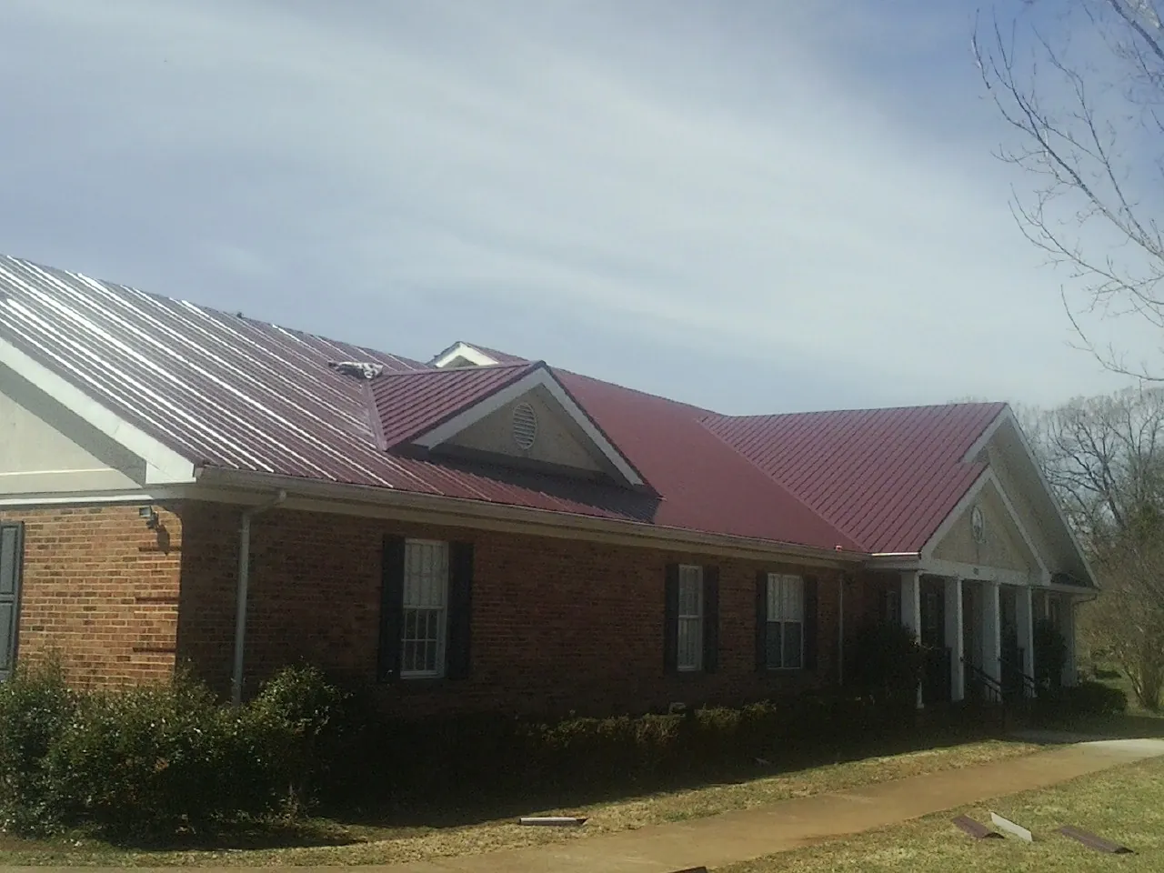 Red metal roof with gabled entries on a long brick building, from a Hail Damage Roof Repair job in Forestdale