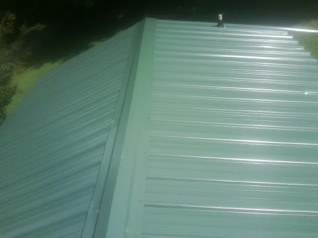 New green metal panels meeting at the ridge of a roof — Flat Roof Repair work by our crew in Forestdale