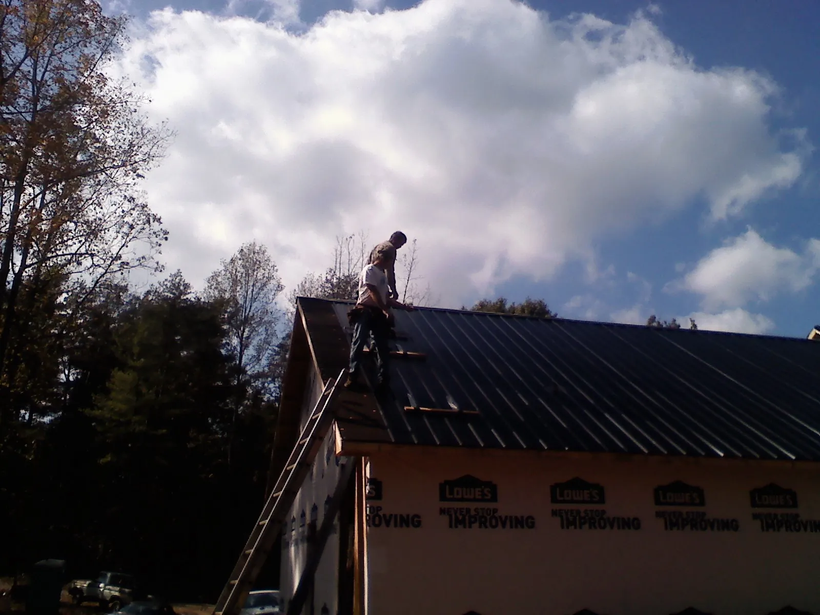 Roofer fastening dark metal panels high against a cloudy sky, from a Roof Inspection job in Forestdale