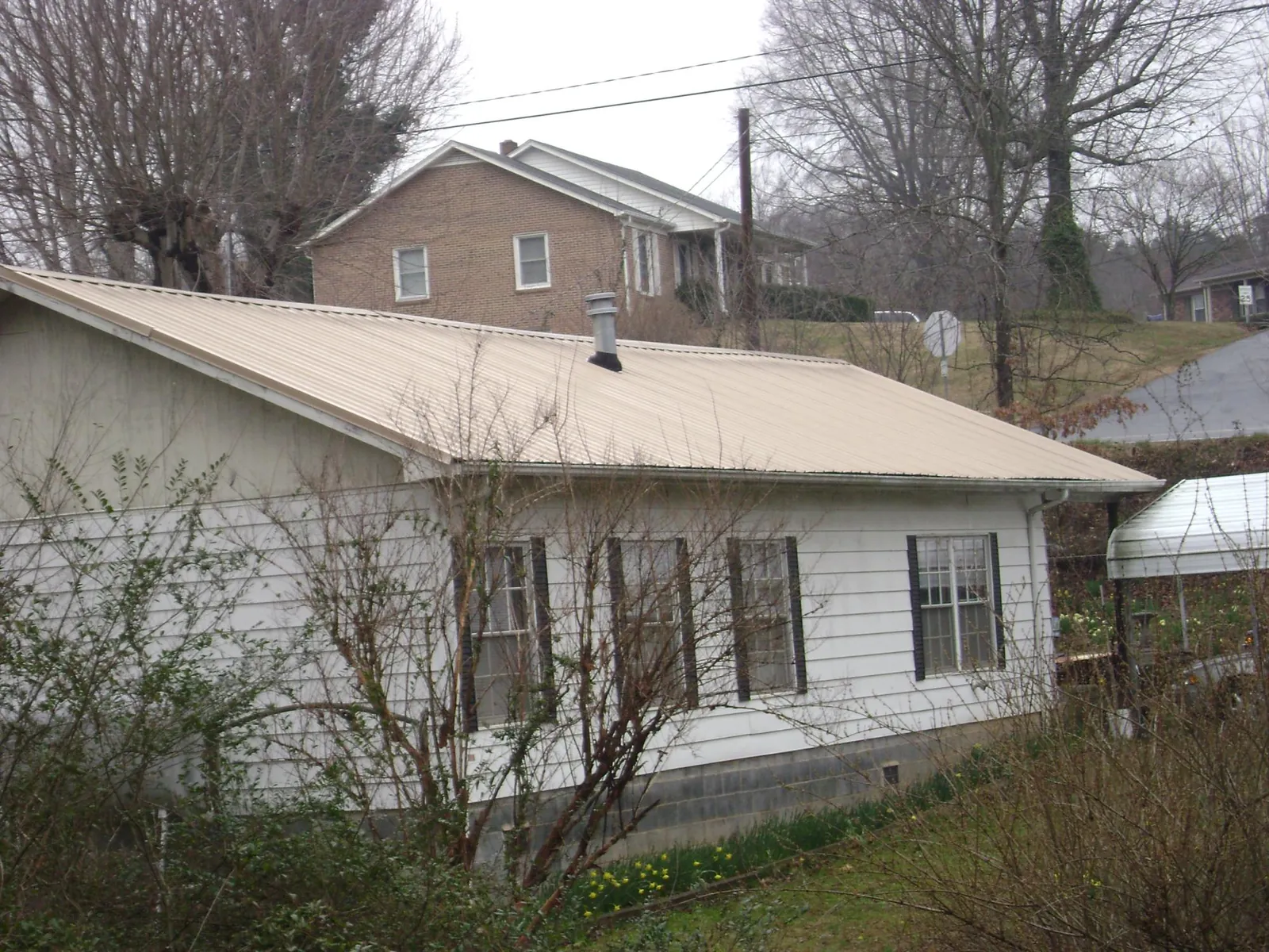 Tan metal roof on a white sided house set into a hillside — Commercial Roofing by Roofing Brothers in Forestdale